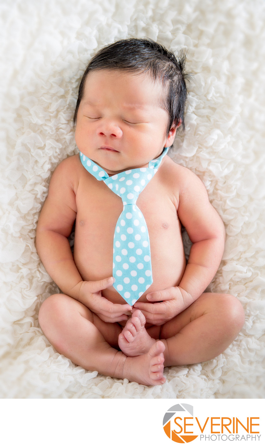 newborn boy with blue tie and white blanket