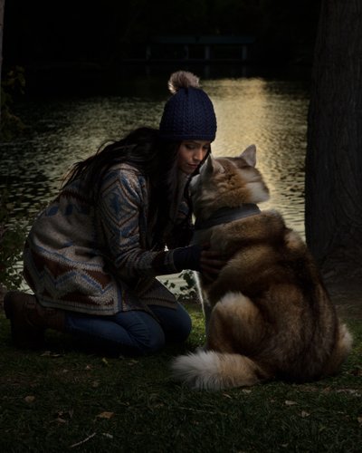 Beautiful woman wearing fall sweater and hat by a pond with her dog