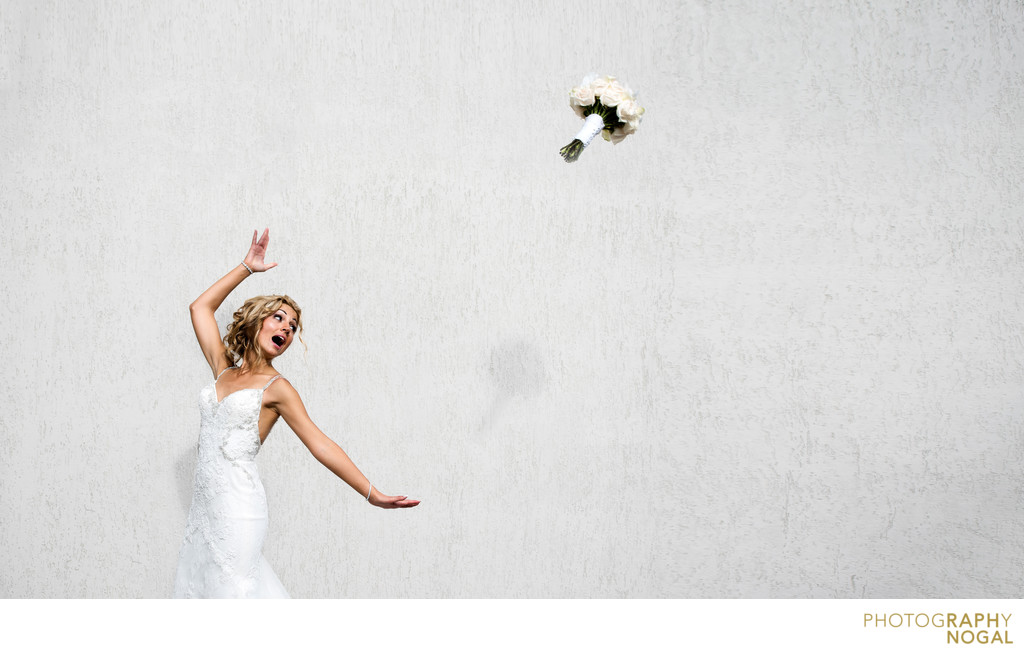 Bride tosses wedding bouquet in front of white wall