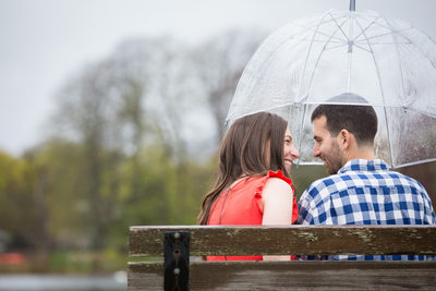 Rainy Engagement Pic of Couple on Bench under Umbrella