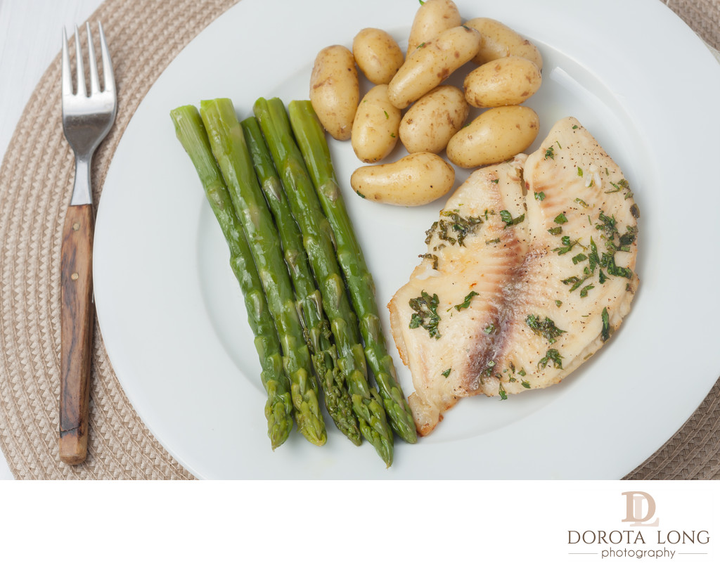 cooked fish with parsley servied with asparagus and baby potatoes on white plate
