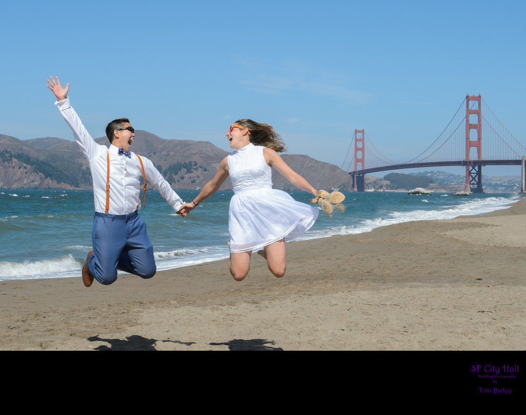 A LGBTQ  Couple jumping at Baker Beach with the Golden Gate Bridge