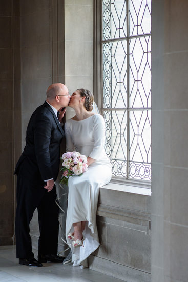 bride and groom kissing in window light at third floor window