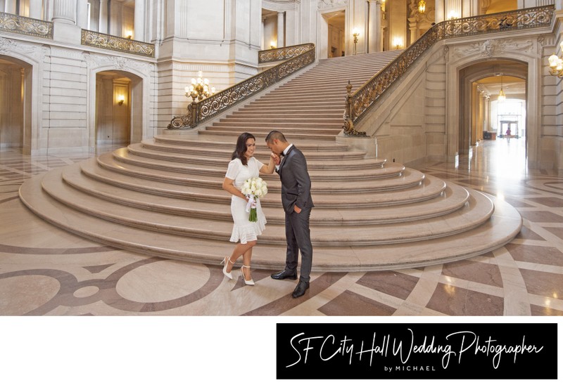 City Hall Groom kisses Bride's hand in front of the Grand Staircase