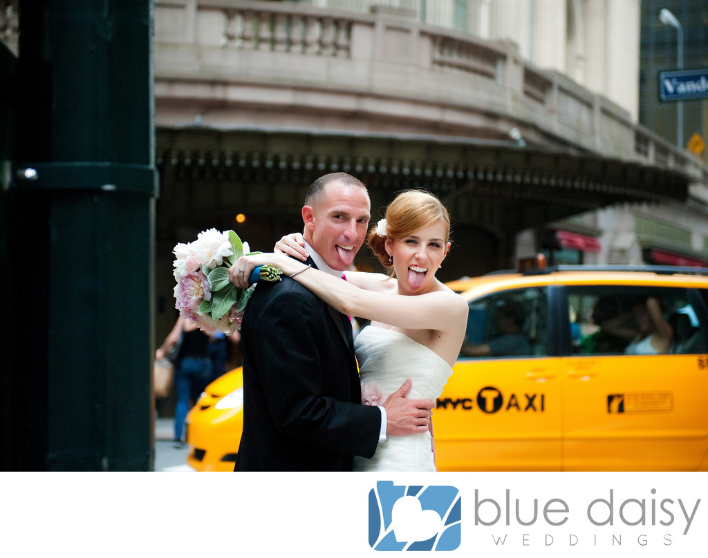 Bride and groom sticking tongue out with yellow cab