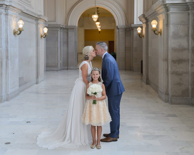 Wedding Kiss over flower girl at San Francisco City Hall