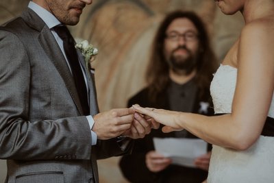 placing the wedding band on his brides finger