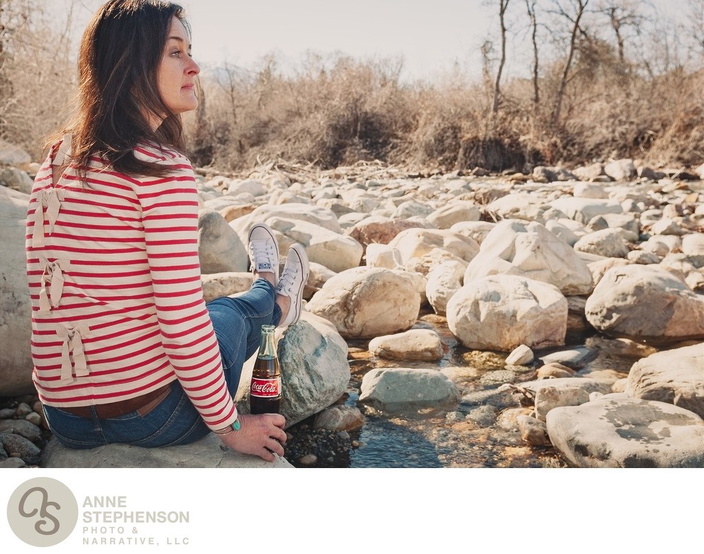 Woman with Coca Cola bottle at edge of a rocky creek
