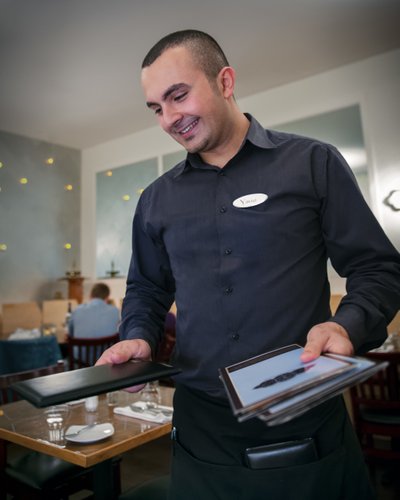 Waiter delivers menu with a smile at Greek restaurant