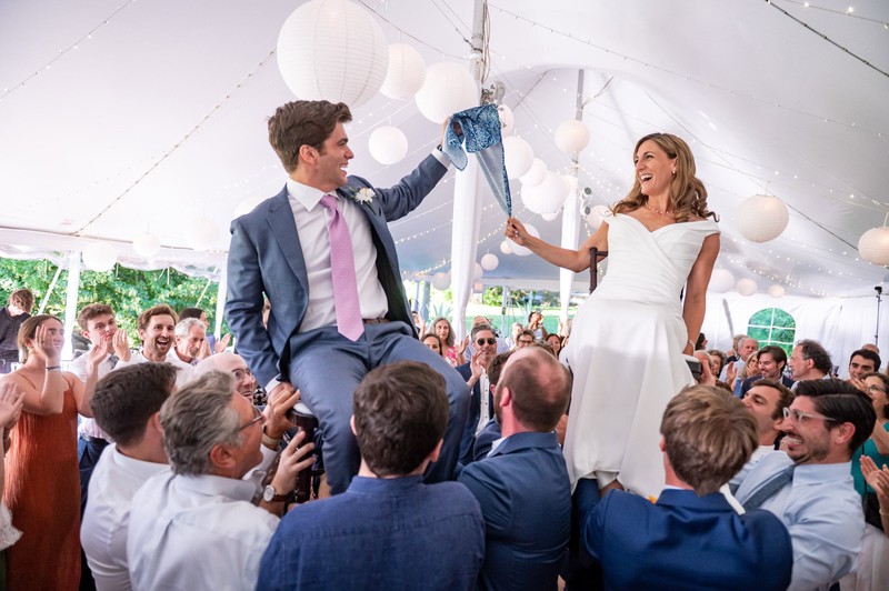 Joyful hora moment between a bride and groom under a beautiful tent