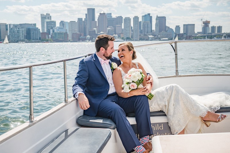 Bride and groom laughing on a boat with the Boston skyline in the background