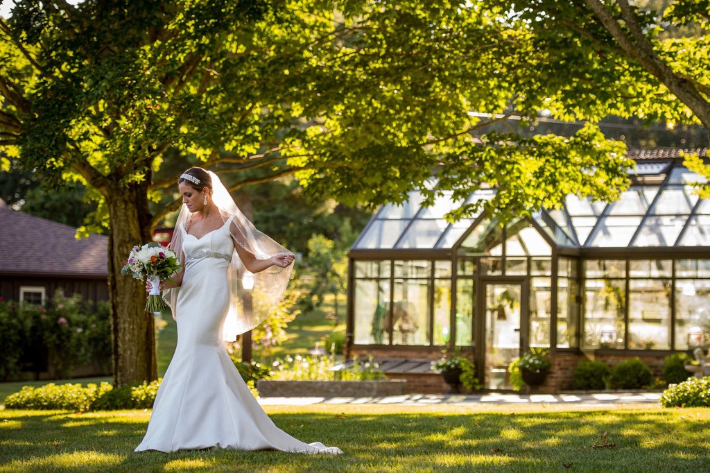 Bride twirls with veil near greenhouse – Fern Hill Barn