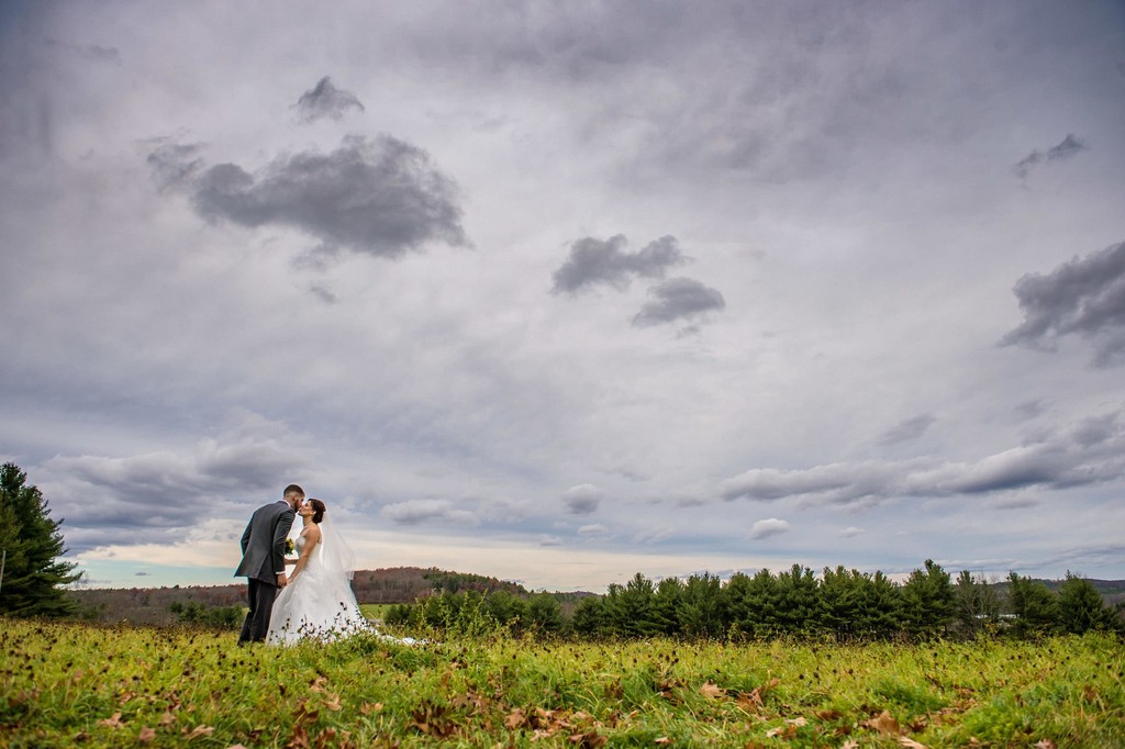 Wide-open field kiss under moody sky – Fern Hill Barn wedding