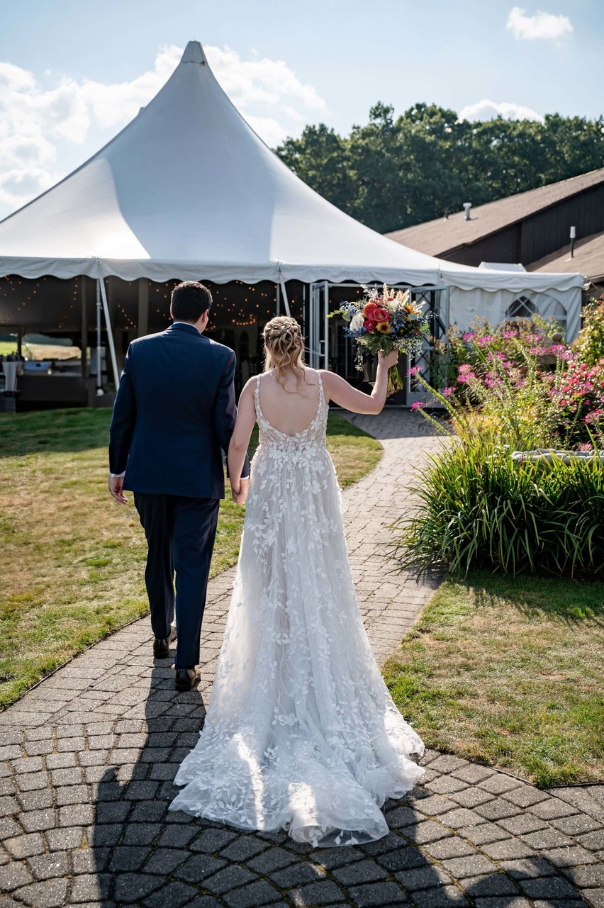Bride and groom walking toward tent – Fern Hill Barn path