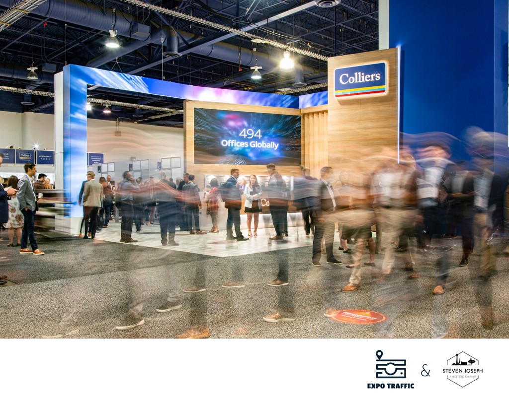 people blurring by the Colliers real estate booth at Las Vegas convention with busy trade show floor and attendees networking
