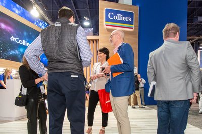 Colliers real estate booth at Las Vegas convention with busy trade show floor and attendees networking