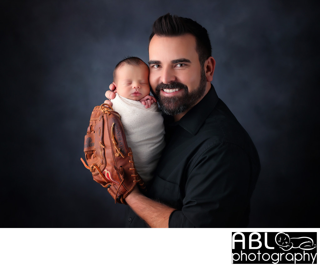 Father holding newborn with baseball glove