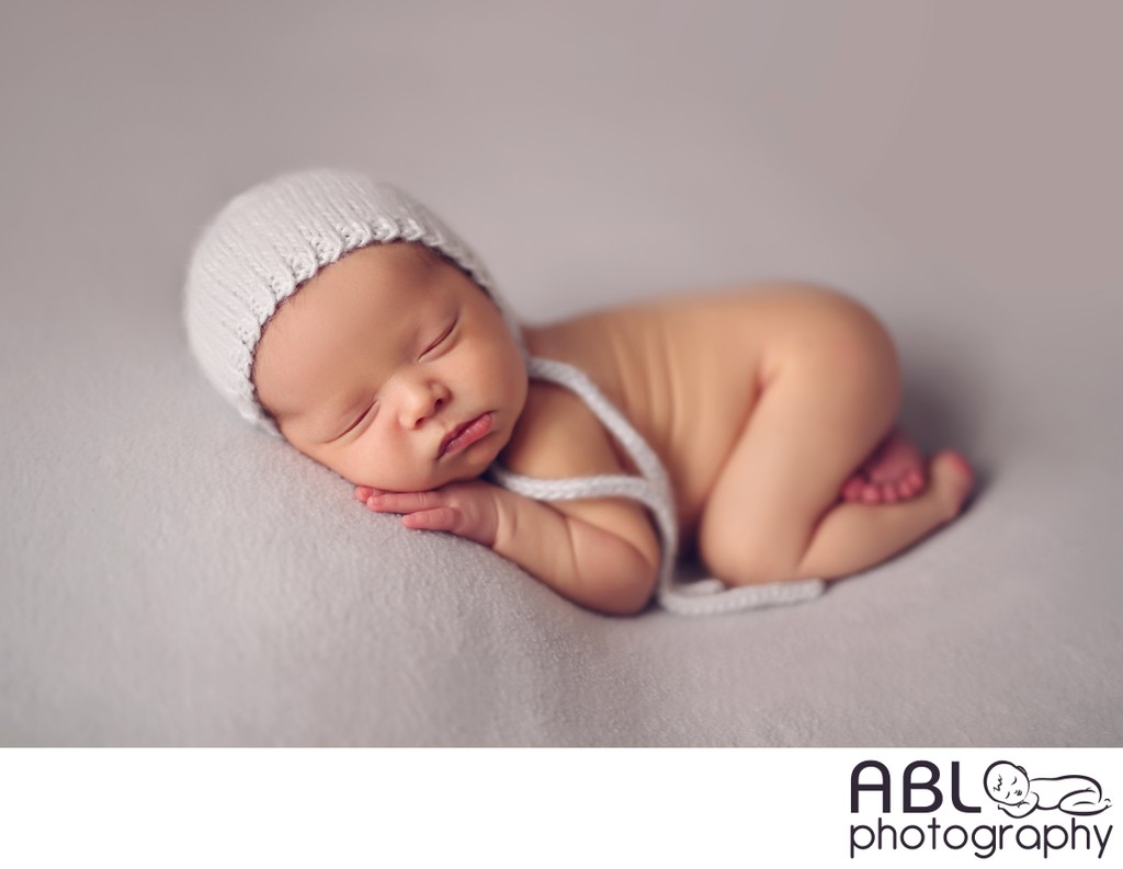 baby boy in knitted bonnet on light gray backdrop