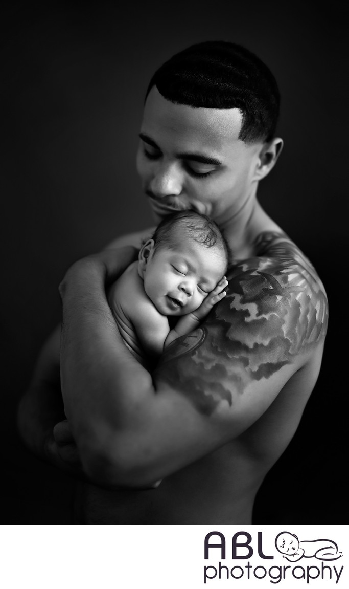 Shirtless father with tattoo holding baby