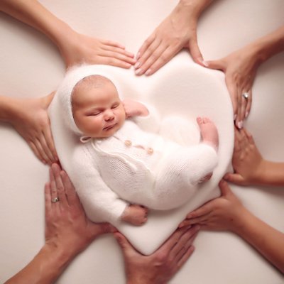 Newborn baby posed in heart prop surrounded by loving hands