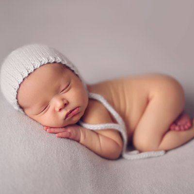 baby boy in knitted bonnet on light gray backdrop