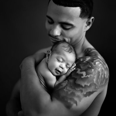 Shirtless father with tattoo holding baby