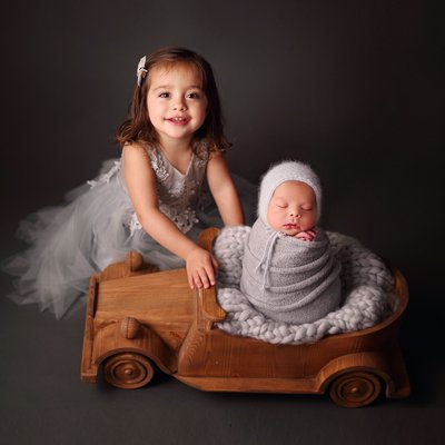 A girl with newborn brother in wooden car