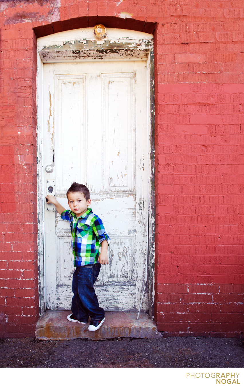 boy opening a white rustic door on red building