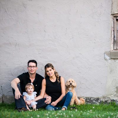 family sitting by rustic wall with baby girl and dog