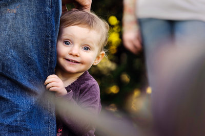 girl peeking around dad's leg and smiling at camera