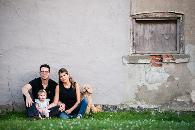 family sitting by rustic wall with baby girl and dog