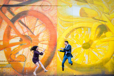 Couple jumping in the air with bike mural behind them