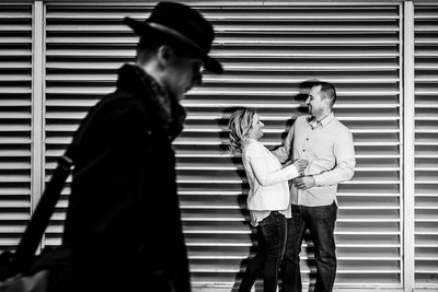 Couple standing as man with hat walks by.