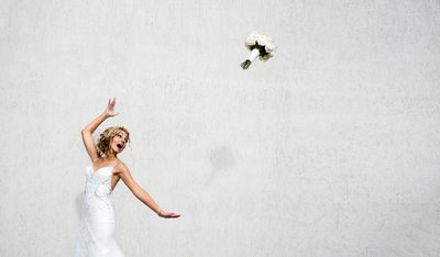 Bride tosses wedding bouquet in front of white wall