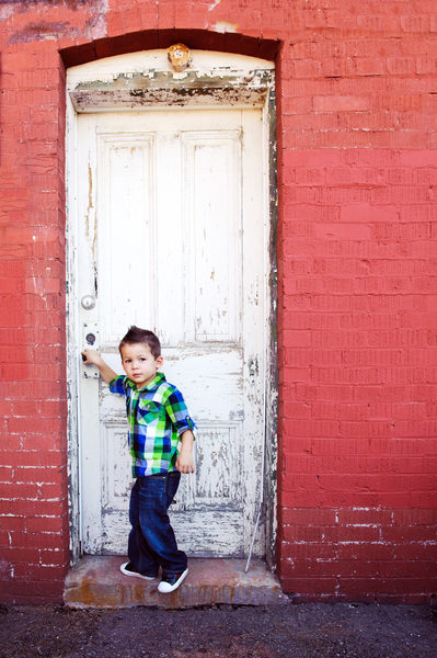 boy opening a white rustic door on red building