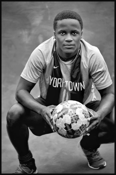 Senior soccer player Pius kneeling holding a soccer ball