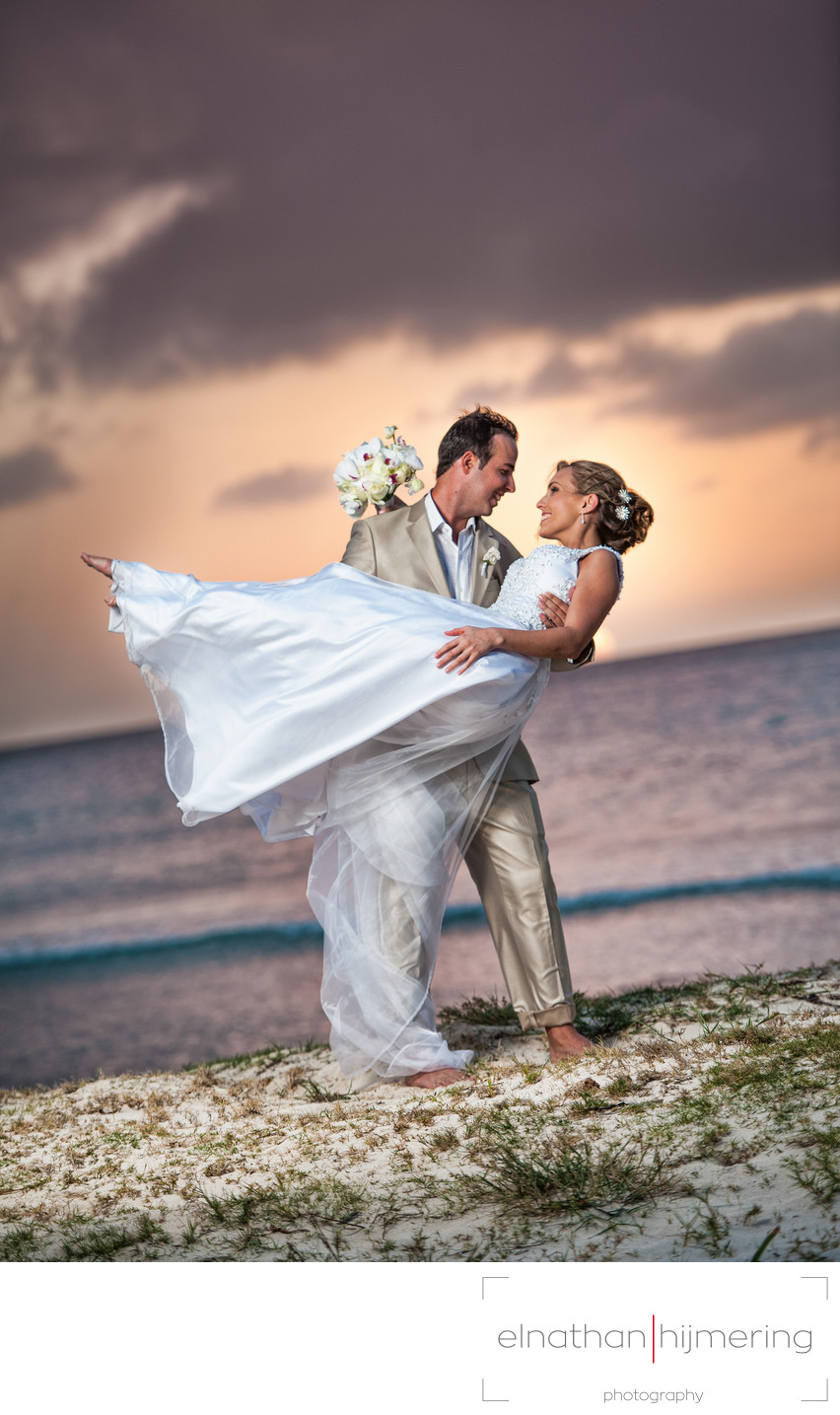 groom picking up bride on beach sunset