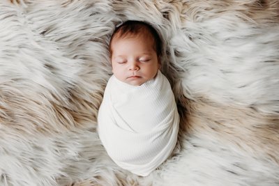 Swaddled newborn sleeping on fuzzy blanket session