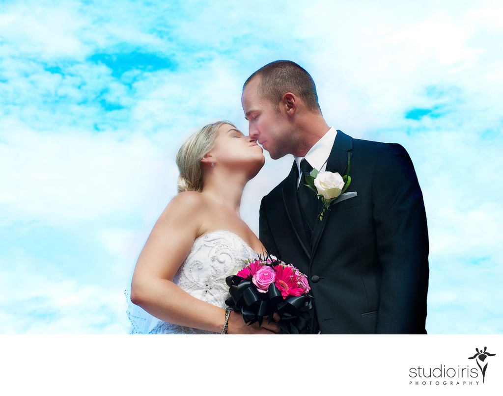 Bride and groom kissing against blue sky at lakeside wedding in Mont-Tremblant, Quebec 