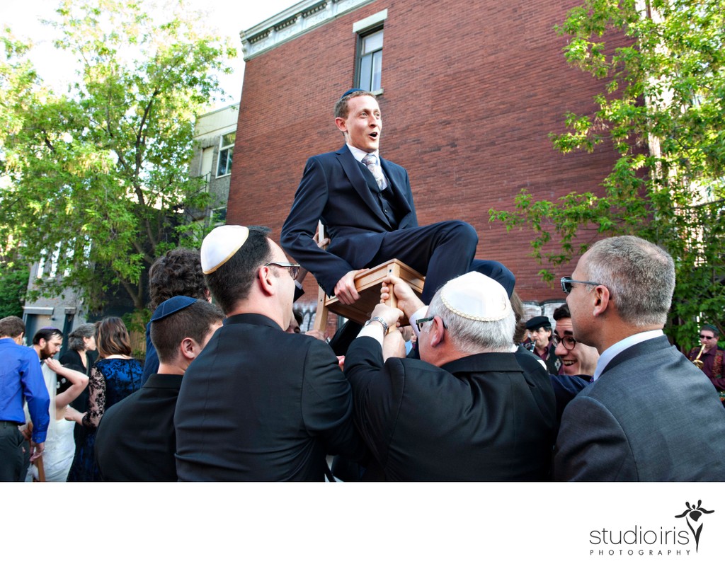 Groom on chair during hora dance outside Bagg Street synagogue in Montreal