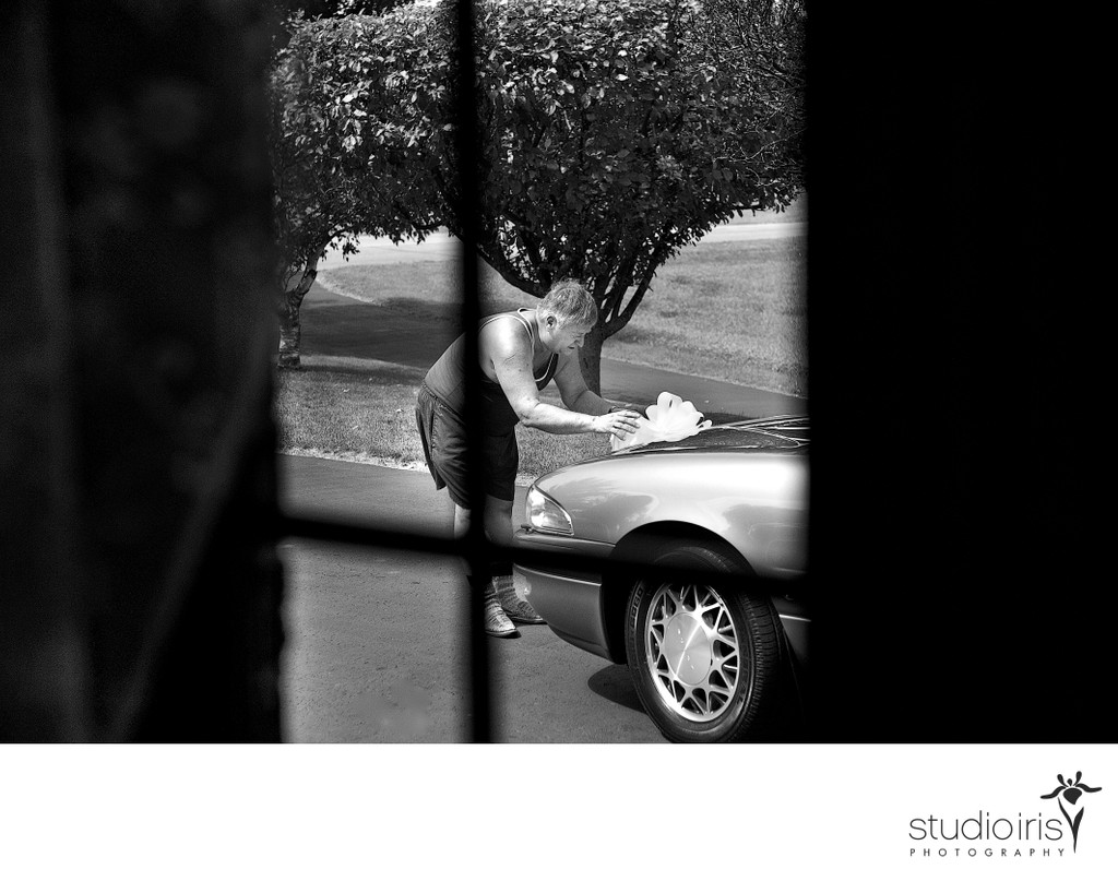 Father of the bride seen through window attaching wedding bow to car 