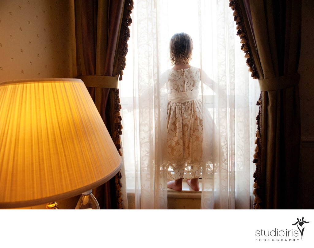 Little girl standing behind curtains on window ledge during Quebec City wedding 