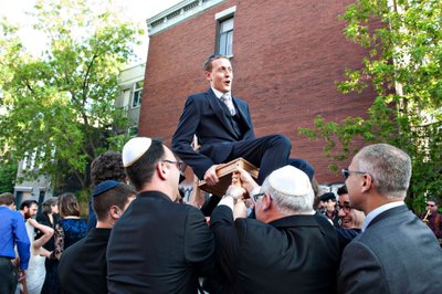 Groom on chair during hora dance outside Bagg Street synagogue in Montreal