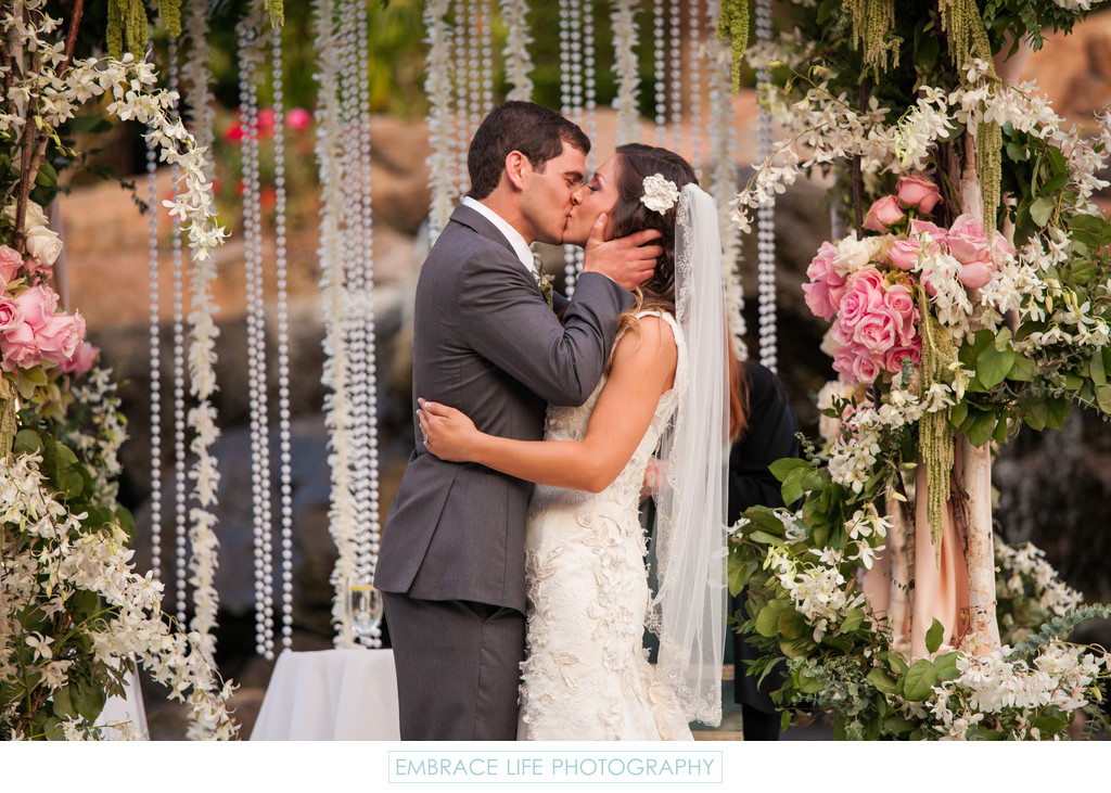 Husband and Wife Share First Kiss Under Floral Chuppah