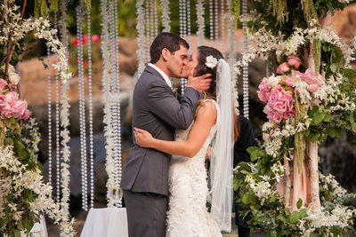 Husband and Wife Share First Kiss Under Floral Chuppah