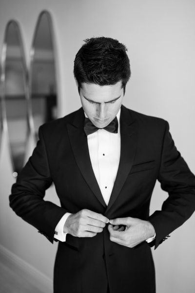 Groom in Black Bow Tie Buttons his Tuxedo Jacket