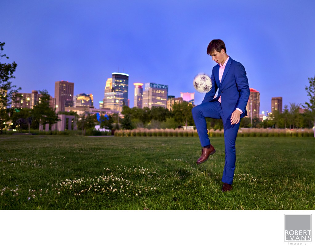 A boy in a suit playing with a soccer ball at dusk