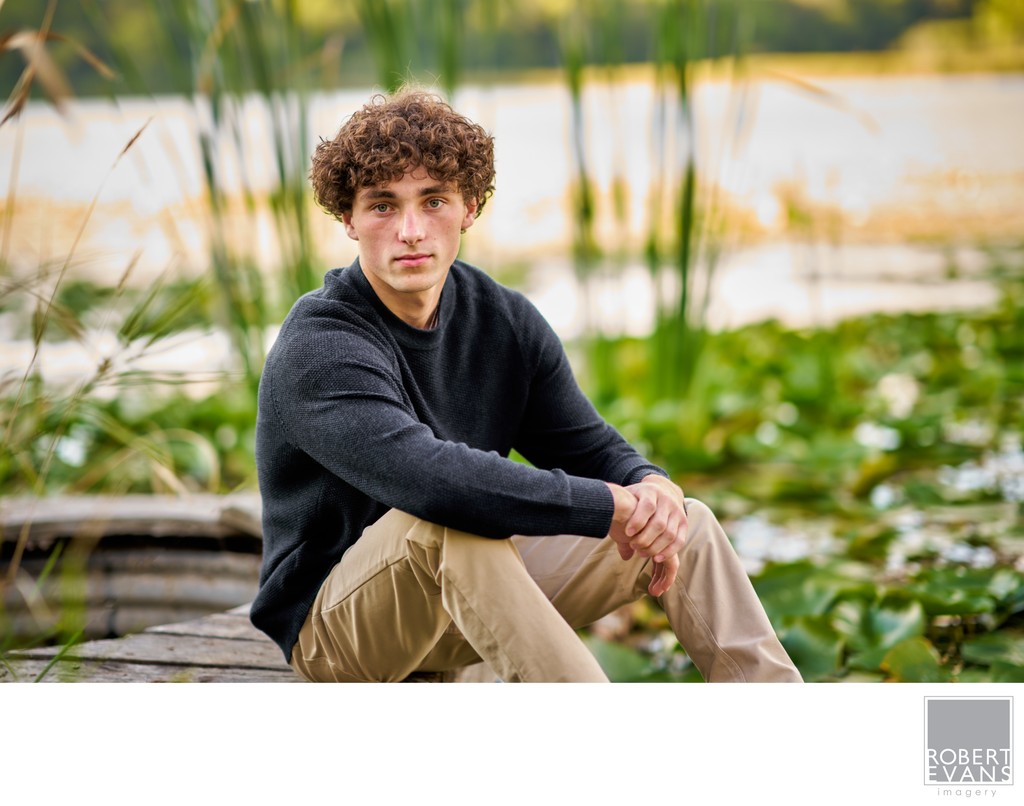 Portrait of a Senior boy sitting on an old dock at the edge of a lake. 