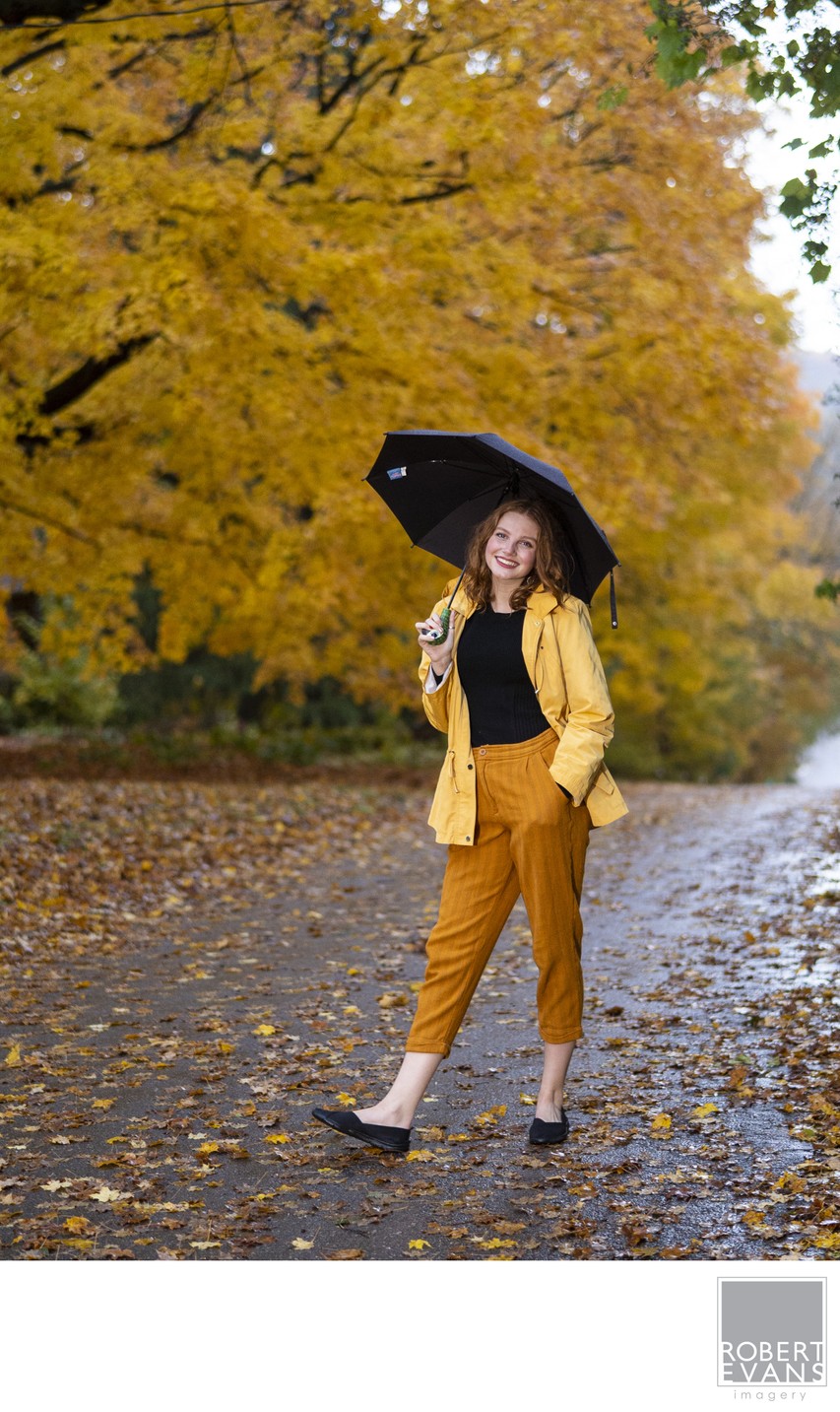 The yellow rain coat, the back umbrella and the yellow leaves on the tree