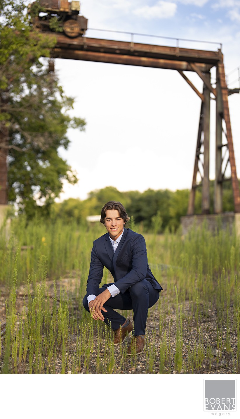 Sharp dressed high school senior boy dressed in a blue suit near an old railroad bridge
